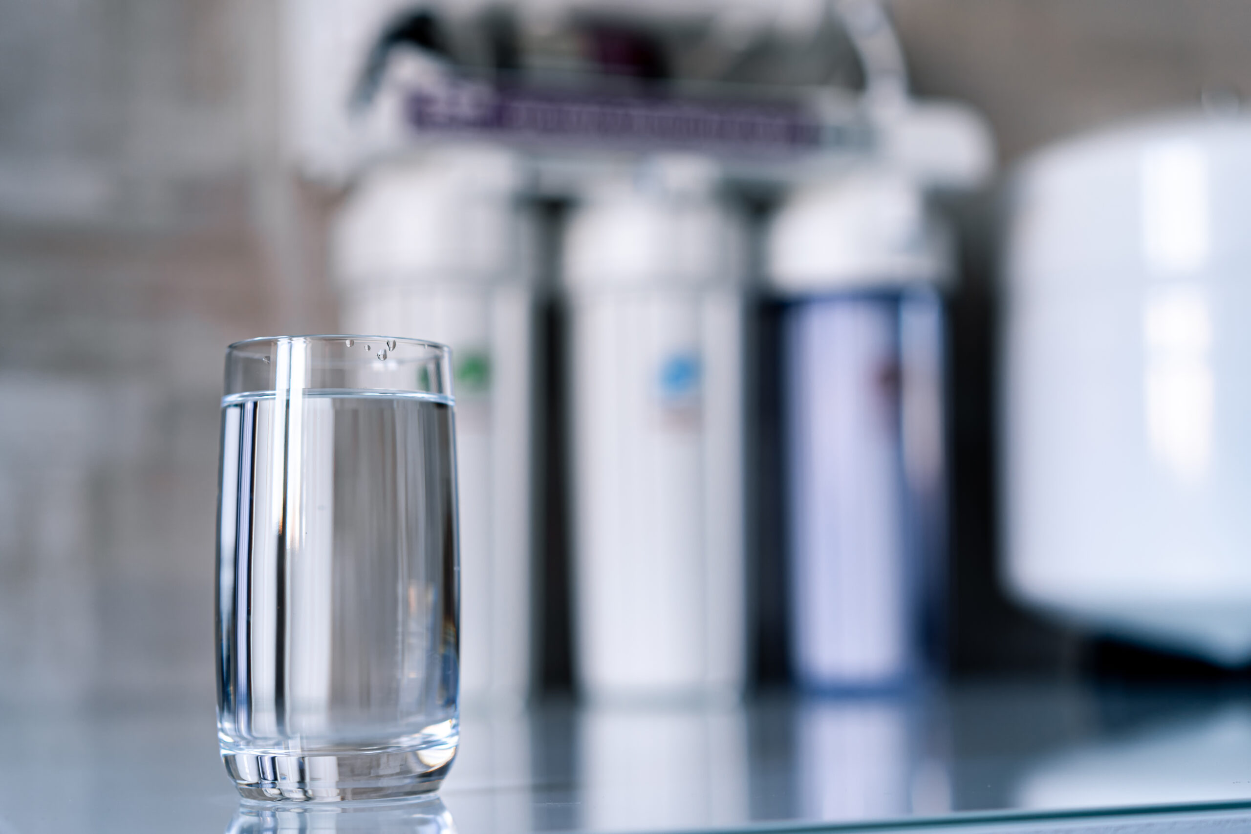 Clean water in glass on a countertop and water filters in the blurred background.