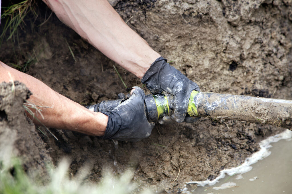 Plumber repairing a sewer line in a trench dug in a yard.